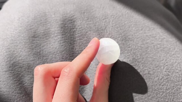 Person rotating a translucent white crystal tumbled stone on a gray background.