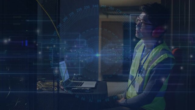 Tech observing rack lights donning red earmuffs typing on laptop for IT checks blue HUD overlays