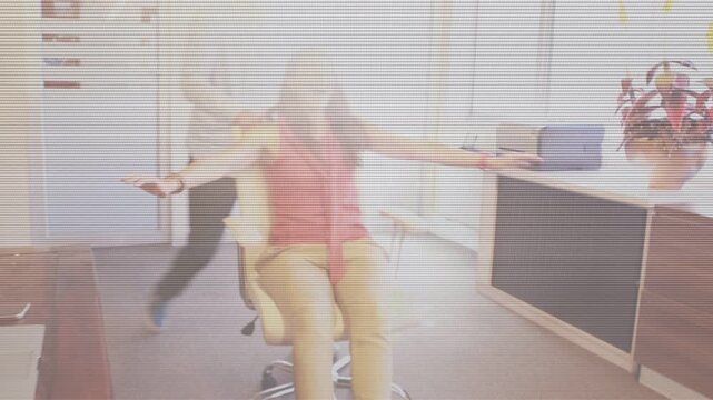 Woman typing on laptop as man pushes rolling chair, woman spinning playfully during office break