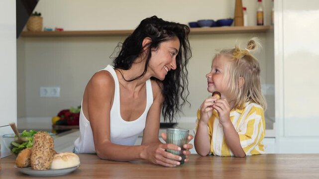 Cute little blonde boy eating chocolate cookie in bright modern kitchen with fresh vegetable salad on table happy child enjoying sweet treat at home