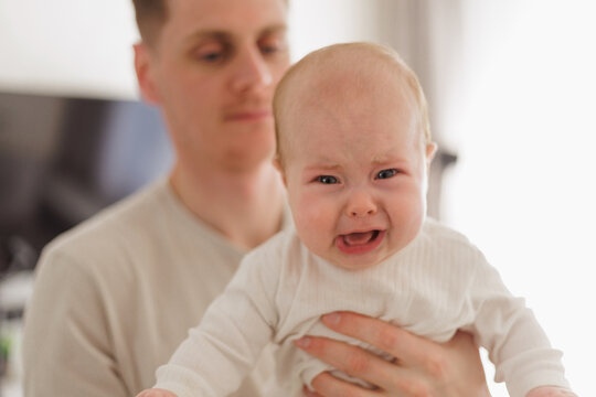 Father holding a crying baby, close-up of distressed infant with red eyes and open mouth