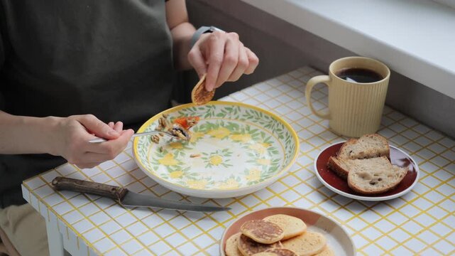 person finishes their breakfast or lunch in kitchen. delicious and healthy food cooked at home. woman eats flatbread pancakes and drinks coffee. vegetarian diet for body health. high quality 4k video
