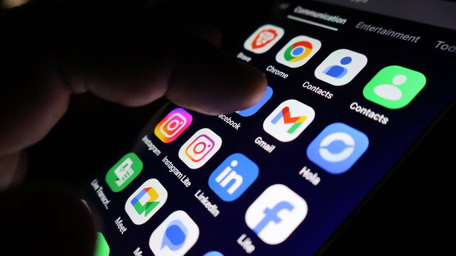 A hand interacting with social media apps on a smartphone screen in the dark