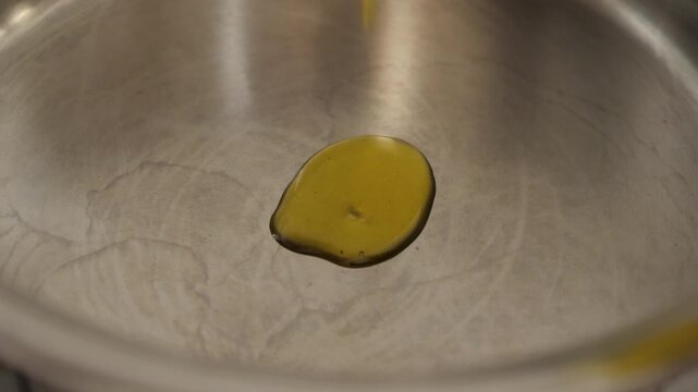 Slow Motion of Extra Virgin Olive Oil Pouring into Pan. Golden Liquid Swirling on Dark Frying Surface - Gourmet Cooking and Healthy Mediterranean Diet Concept.