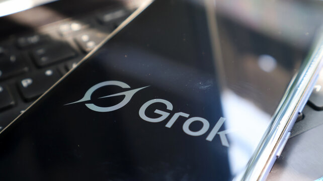 A close-up view of a laptop screen displaying the Grok logo on a blurred background