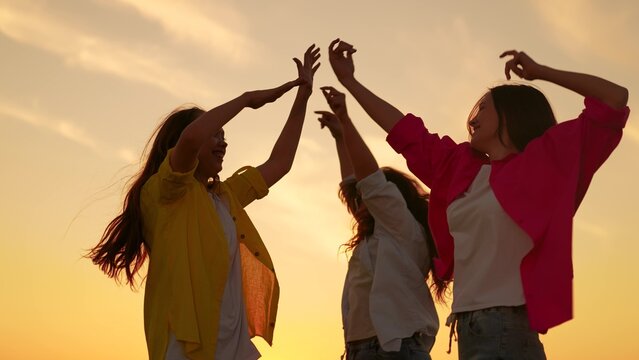 Young women having fun in nature, relaxing in nature. People girls dancing to music at beach party raising hands up. Party, celebration, dancing, group of happy people raising hands to sky in evening.