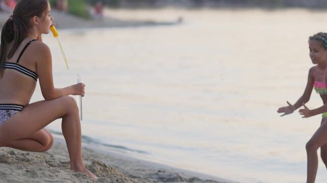 Funny girl catches bubbles on the shore of the lake, which her older sister lets go