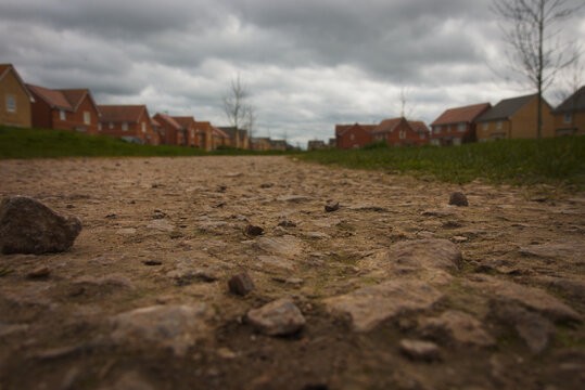 Peterborough, Cambridgeshire, England, UK - March 24th 2026: Low to the ground shot of Hampton Water rural path. Dramatic clouds, stony path, budding trees and houses on each side.