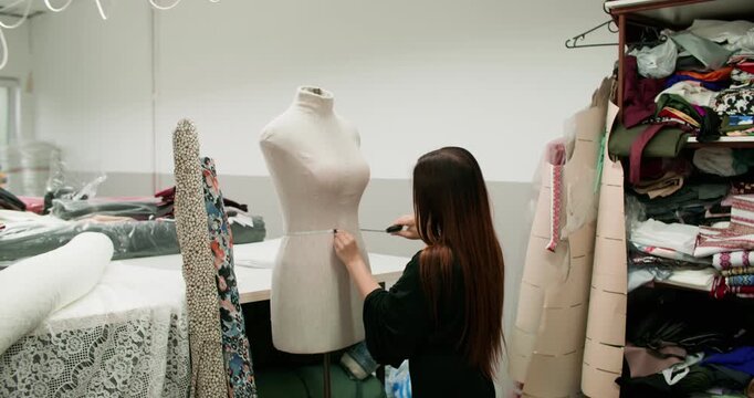 Couturier work. Fashion business. Woman measuring size dimensions of mannequin figure with tailor tape for sewing in atelier interior.