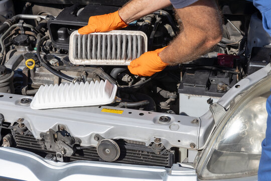 Mechanic replacing dirty engine air filter with clean new filter during car maintenance service inspection