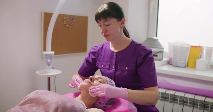 Skin cleansing. Detox procedure. Female beautician using cotton pads from client face removing moisturizing beauty mask in clinic.