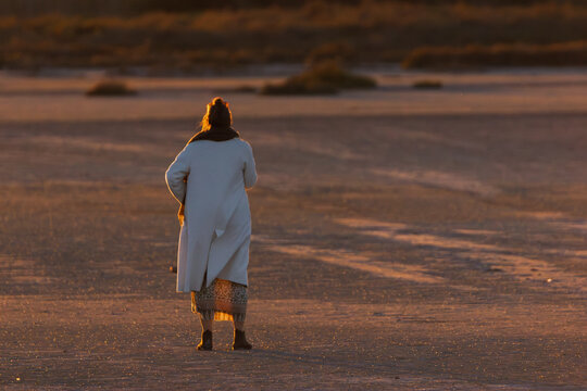Femme de dos seule sur sol sableux au coucher du soleil, ambiance de solitude et r&eacute;flexion