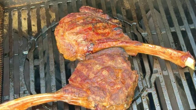 Large pieces of tomahawk meat cooking on a grill