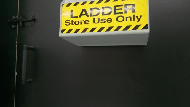 Yellow ladder store use only safety sign on dark door