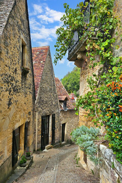 Narrow cobblestone street in the village of Beynac-et-Cazenac, Dordogne, France with medieval stone houses and ivy covered balcony