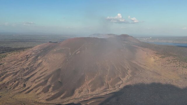 Smoke and ash rise from a volcano in Nicaragua as sunlight shines on the landscape. The area shows signs of volcanic activity and rugged terrain.