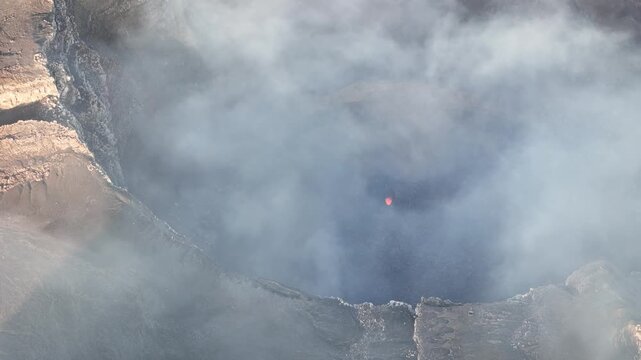 Watch the aerial view of a volcano crater. Smoke rises as the lava glows from below. The view shows the raw power of nature in the evening light.