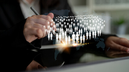 Business professional using digital tablet for global communication and connection with people icons and world map representation in a modern office setting Quark. © InfiniteFlow