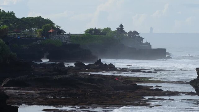 Rugged Rock Stacks With Pounding Surf, Breaking Against Jagged Outcrops, Misty Spray And Foam, Distant Temple Silhouette On Clifftop, Raw Coastal Energy And Exploration Vibe, Tanah Lot temple, Bali