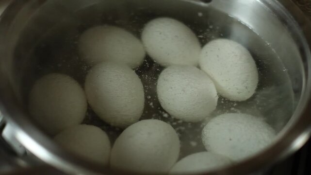 Eggs are boiled in water in a metal pan on the stove.