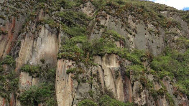 Approaching a cliff with grey, brown and red colors that is covered in grass and bromelias