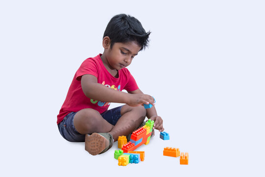 Adorable young boy sitting on the floor and playing with colorful building blocks