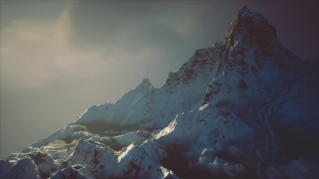 Snow covered peaks dominate the landscape, illuminated by the fading light of sunset. A misty ambiance surrounds the rugged mountains, enhancing their majestic beauty.
