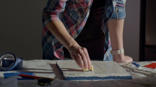 Close up of woman creating relief texture on canvas using sponge and paste. Concept of abstract art process