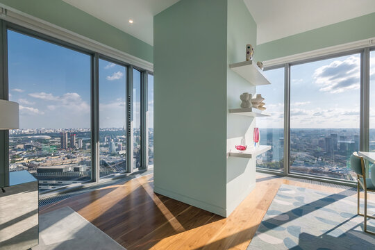 People can see a city skyline from a modern apartment with large windows. Sunshine fills the room and bright colors create a lively space