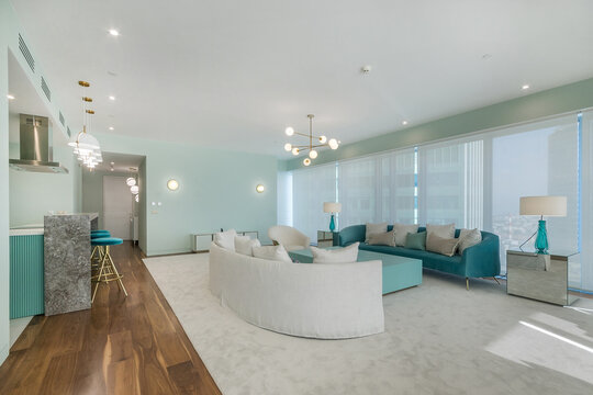 A modern living room in a high-rise apartment. There are large windows letting in light and comfortable furniture arranged for gathering. The room is designed for relaxation