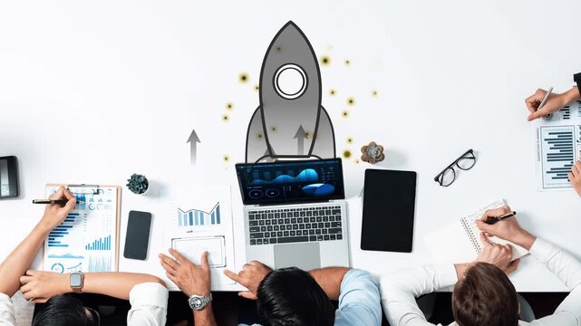 A business team works collaboratively on a project, featuring a laptop and creative rocket illustration, representing growth, innovation, and productivity in the workspace. Raster