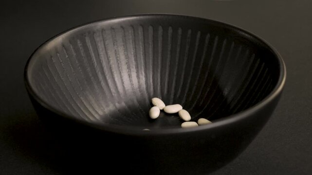 White_beans_falling_into_black_bowl_on_black_background_4k_10bit_120fps