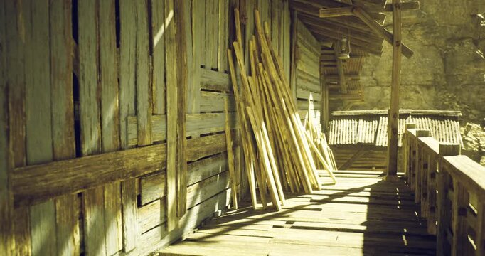 Sticks are leaning against a wooden wall beside a rustic pathway illuminated by warm sunlight. The essence of tranquility and craftsmanship is evident in this serene setting.