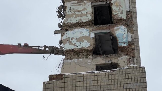 Hydraulic excavator rotating demolition head breaking brick wall of old residential building with falling debris during urban building demolition. High quality 4k footage