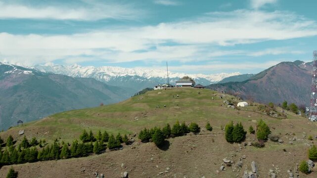 Bijli Mahadev hilltop in Himachal Pradesh with temple complex, telecom tower, and snow mountains, popular travel destination
