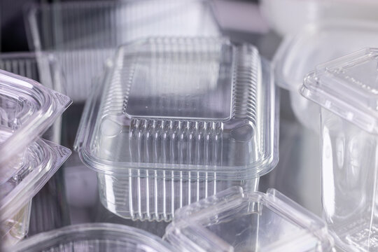 Clear disposable food containers made of plastic, photographed in close-up style, on a reflective surface, representing packaging and sustainability