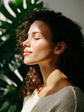 Serene Young Woman Enjoying Sunlight with Closed Eyes Amidst Greenery