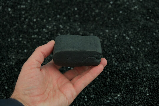 Male hand holding black SBR synthetic rubber chunk on black polyethylene granule background. Styrene-Butadiene Rubber piece. Copolymers