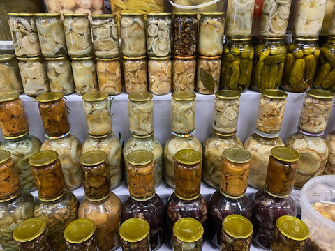 Pickled mushrooms in glass jars at market dangerous homemade canned food. No labels or expiration dates. Unsafe storage conditions. Risk of botulism poisoning. Suspicious preserves at farmers market