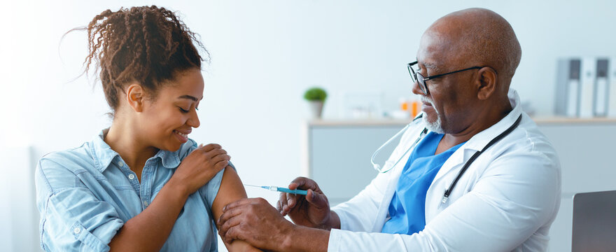 A woman sitting in a clinic smiles as a doctor administers a vaccine to her arm. The doctor wears a stethoscope and looks professional. Soft light fills the room.