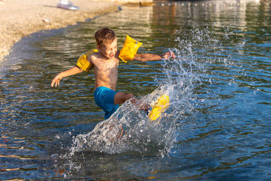 Playful child runs shallow sea water create bright splash warm sunlight summer vacation. Joyful moment show energetic movement, yellow armbands safety carefree childhood fun near beach shore