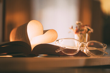 Open book displays heart-shaped pages with glasses nearby, symbolizing love for literature and the pursuit of knowledge in a cozy reading space © Jam