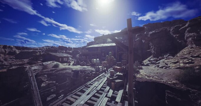 An old mining town is visible with wooden buildings and scattered crates against a backdrop of rocky terrain and a striking azure sky. Bright sunlight illuminates the scene.