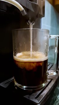 Hot coffee is poured into a glass mug. Frothed milk follows, creating layers and crema. The process shows the rich colors and textures blending together.