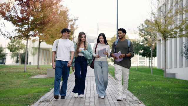 Group of diverse college students walking and talking on a university campus path, carrying notebooks and wearing backpacks
