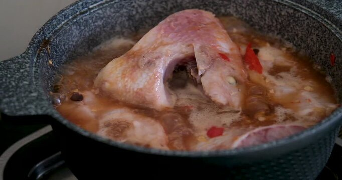 Vietnamese red fish cooking in gray pan with chili garlic and salt simmering on gas stove showing traditional soup preparation step by step