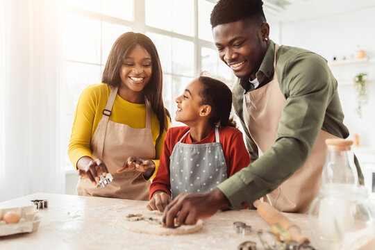 A family is gathered in a bright kitchen to bake cookies. They are using cookie cutters on rolled dough while enjoying their time together. Laughter fills the space as they share the moment.