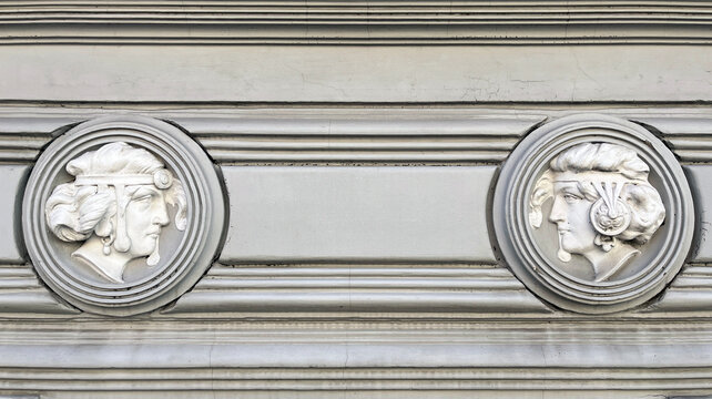 Two classical sculpted heads in circular medallion reliefs embedded in a historic facade, showcasing neoclassical architectural ornament, symmetry, and refined decorative craftsmanship