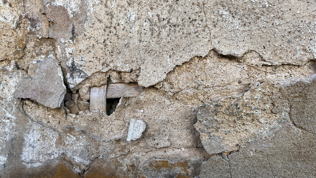 Close‑up of a damaged plaster wall with deep cracks, crumbling layers, and exposed wooden lath beneath the surface, showing heavy weathering and structural decay