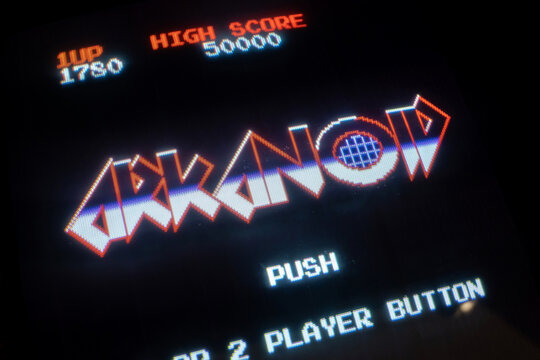 Arkanoid arcade game title screen on CRT display, extreme closeup of classic retro video game start menu with high score and glowing pixel text, vintage arcade machine nostalgia concept, no people